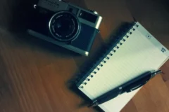 Camera and notepad on a desk, representing writing image alt text