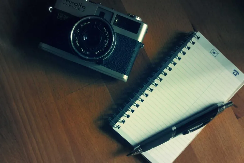 Camera and notepad on a desk, representing writing image alt text